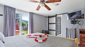 Un dormitorio con cama, ventilador de techo, televisor y vistas al exterior.