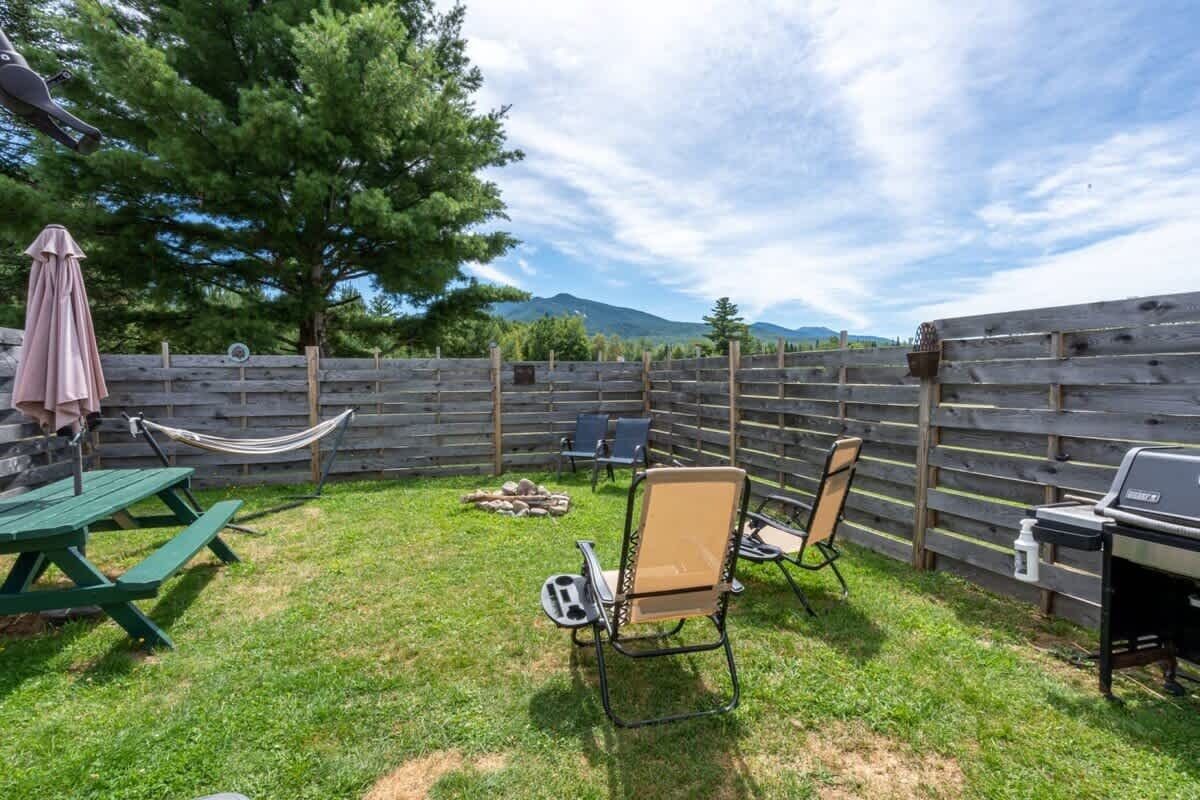 Un jardin avec une table de pique-nique, deux chaises, un hamac, un barbecue et une clôture en bois.