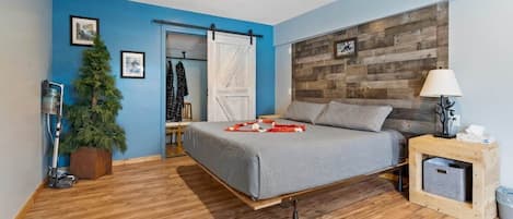 A bedroom with a bed, a wooden headboard, a nightstand, a lamp, a trash bin, a sliding door, and a small plant.