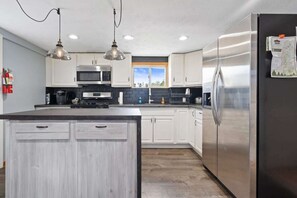 A modern kitchen with white cabinetry, stainless steel appliances, and pendant lighting.