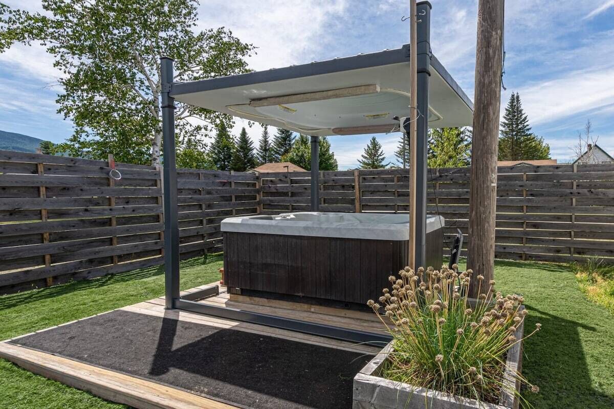 Een hottub met een zonnescherm, omringd door een houten hek en een plantenbak met planten.