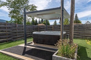 Un jacuzzi con toldo, rodeado por una cerca de madera y un macetero con plantas.