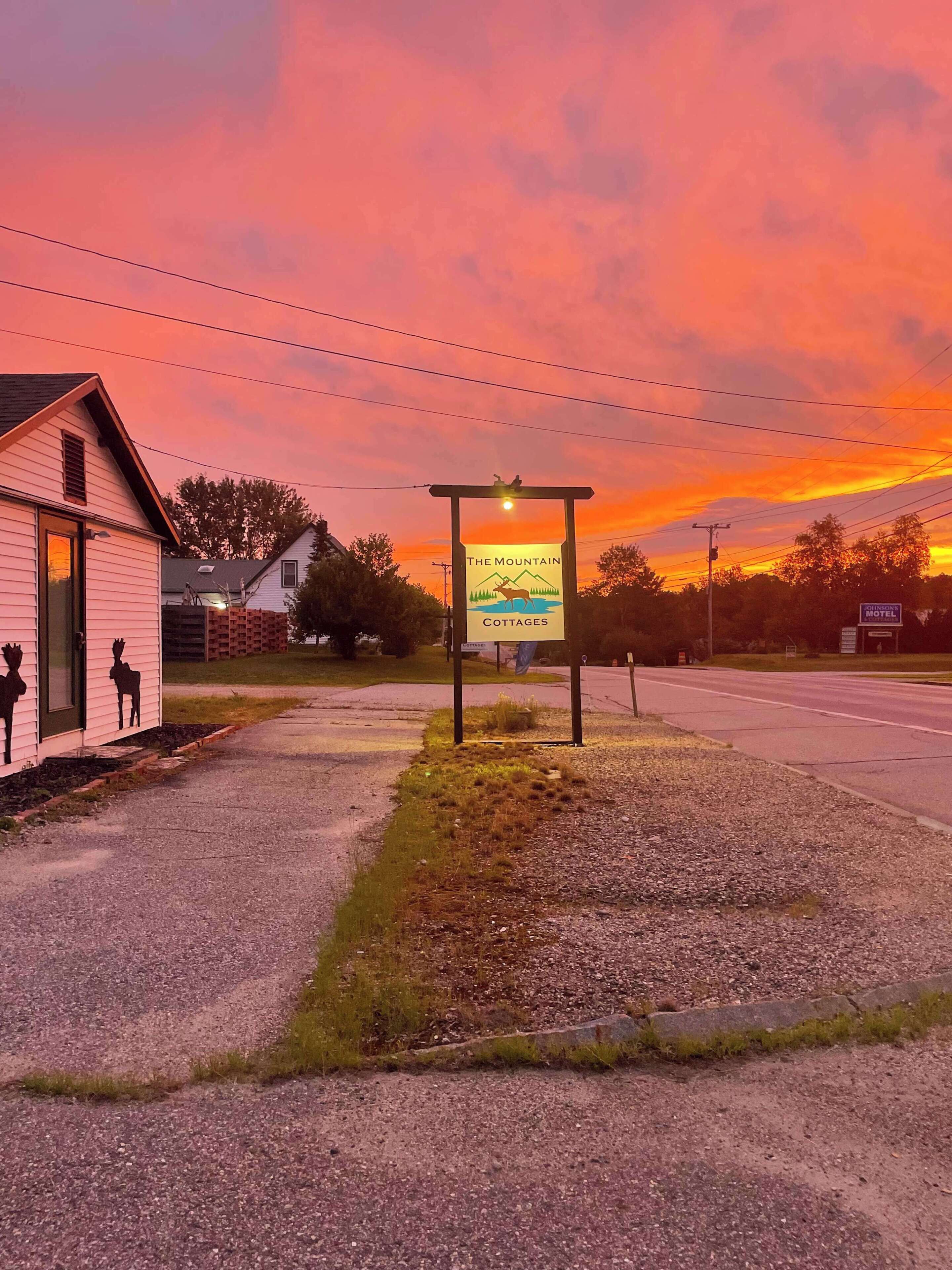 A sign for The Mountain Cottages Motel with a clear view of the surrounding area, including a small building with a door and windows, and a road in the background.