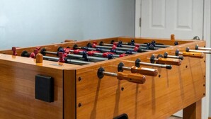 Una mesa de futbolín de madera con múltiples barras y figuras, un panel de control negro y una sección empotrada en el lateral.