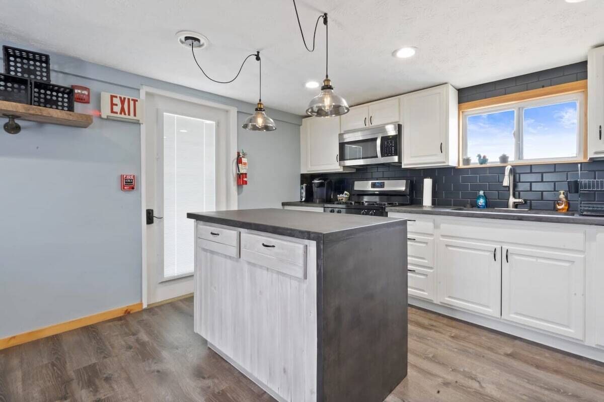 A modern kitchen with white cabinetry, a central island, stainless steel appliances, and pendant lighting.