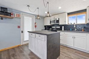 Una cocina moderna con armarios blancos, una isla central, electrodomésticos de acero inoxidable e iluminación colgante.