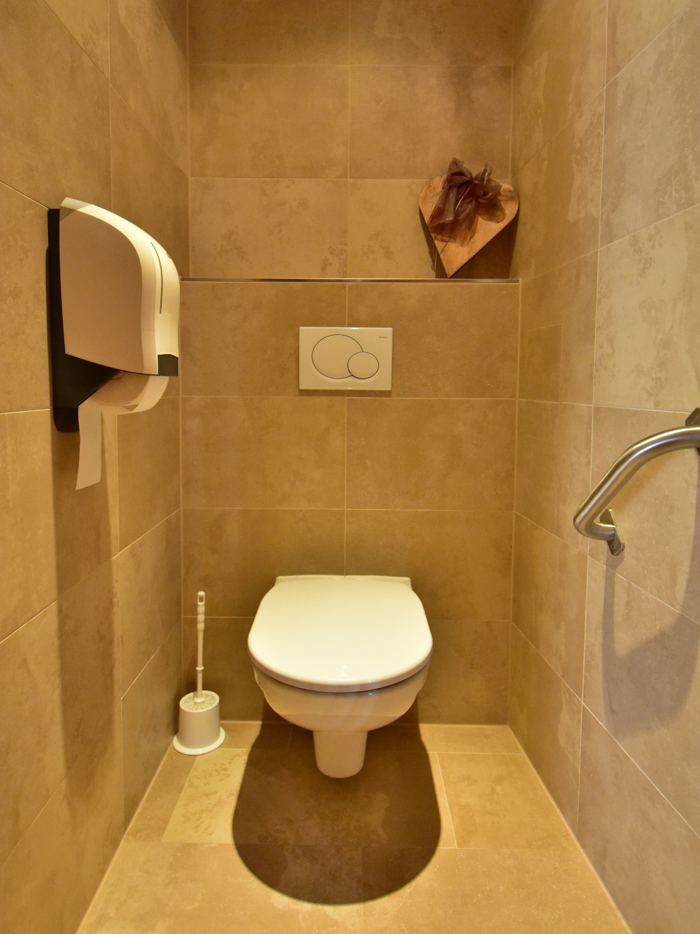 A small, modern bathroom with a toilet, a hand dryer, and a toilet paper dispenser mounted on the wall.