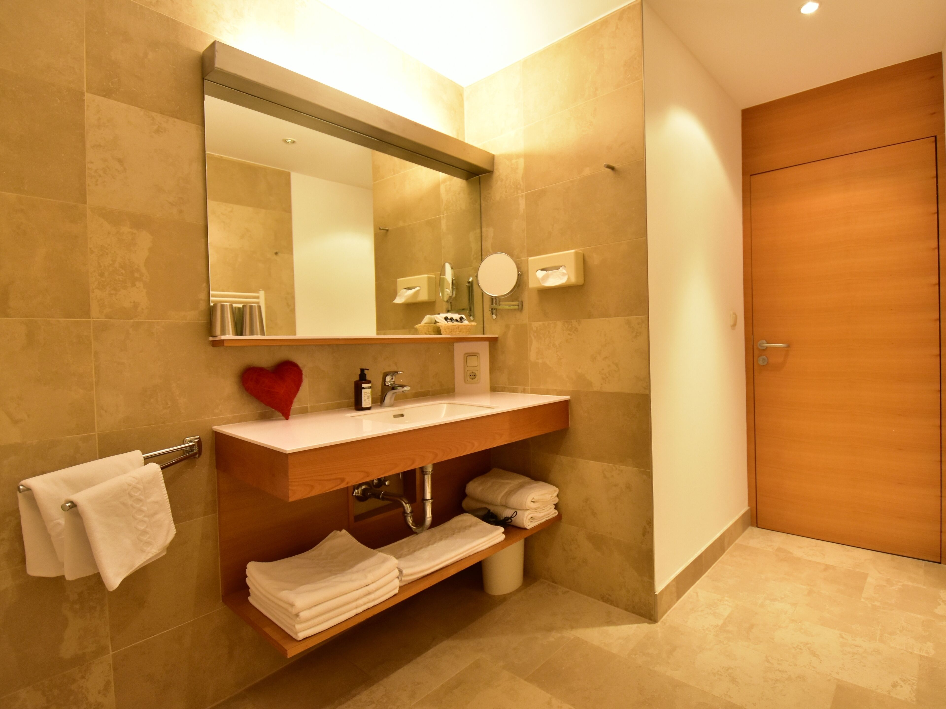 A modern bathroom with a wooden vanity, a large mirror, and a towel rack.