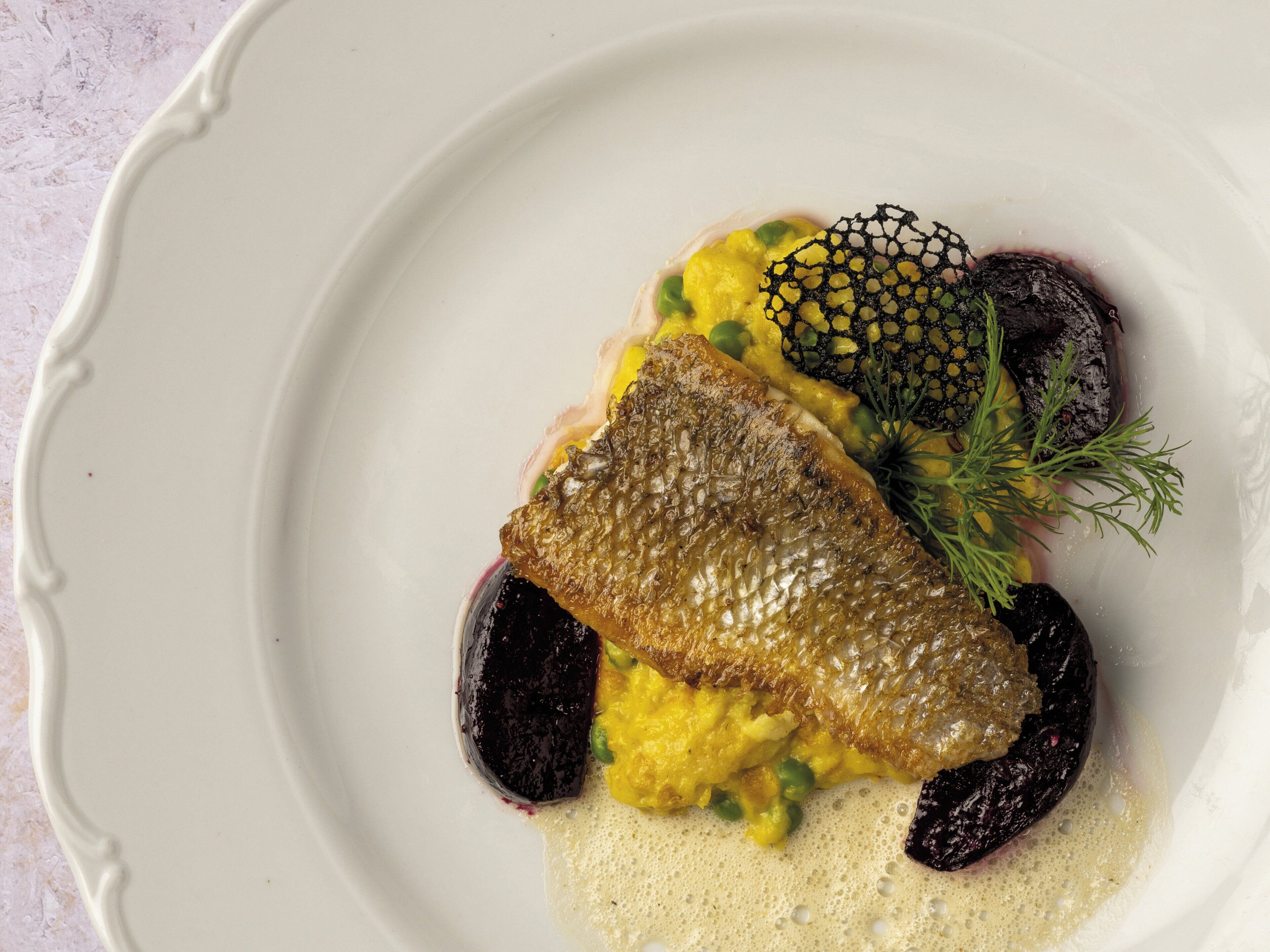 A white plate with a fish, peas, and a decorative element.
