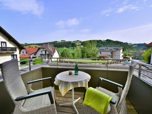 Un balcon agrémenté de meubles en osier, une petite table ronde et une vue sur un paysage verdoyant parsemé de maisons.