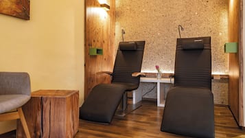 Relax in a serene spa room with two reclining chairs, a small table, and a potted plant.