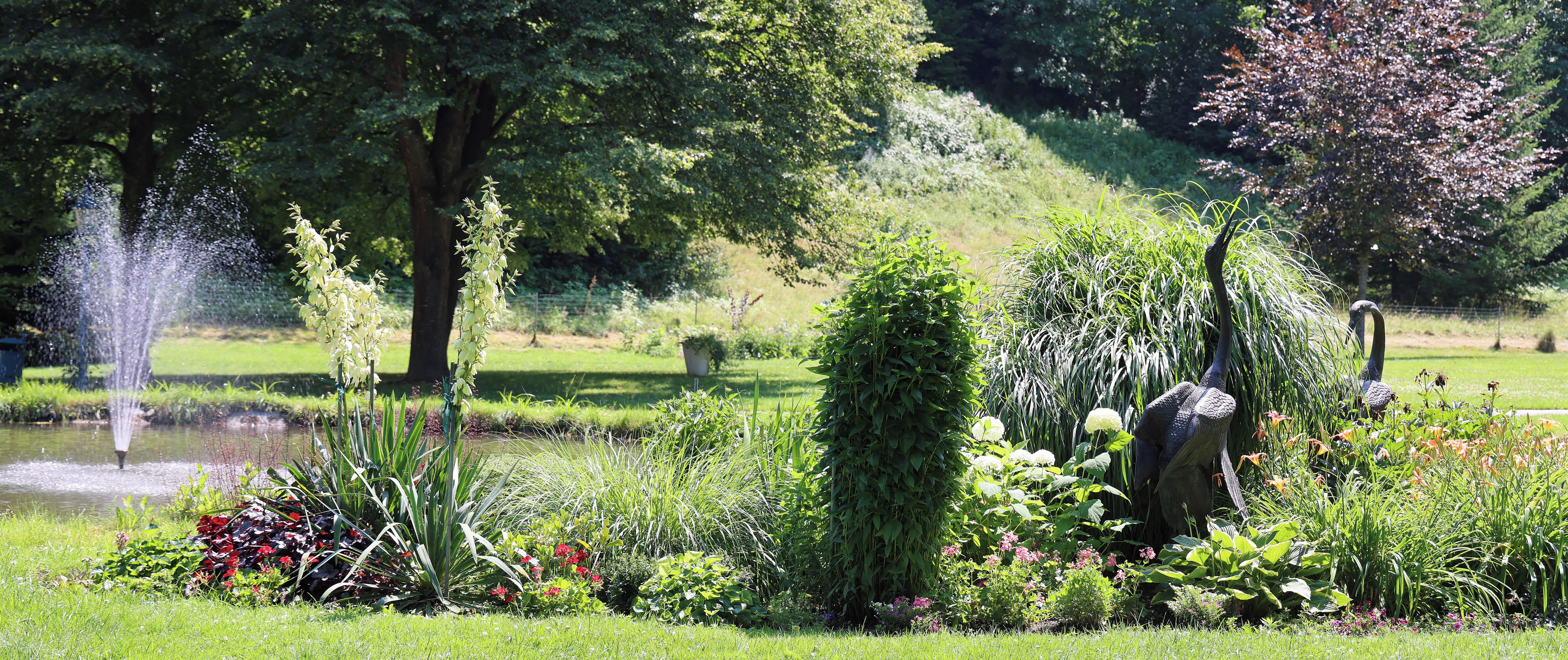 A garden with a fountain, various plants, and a statue.