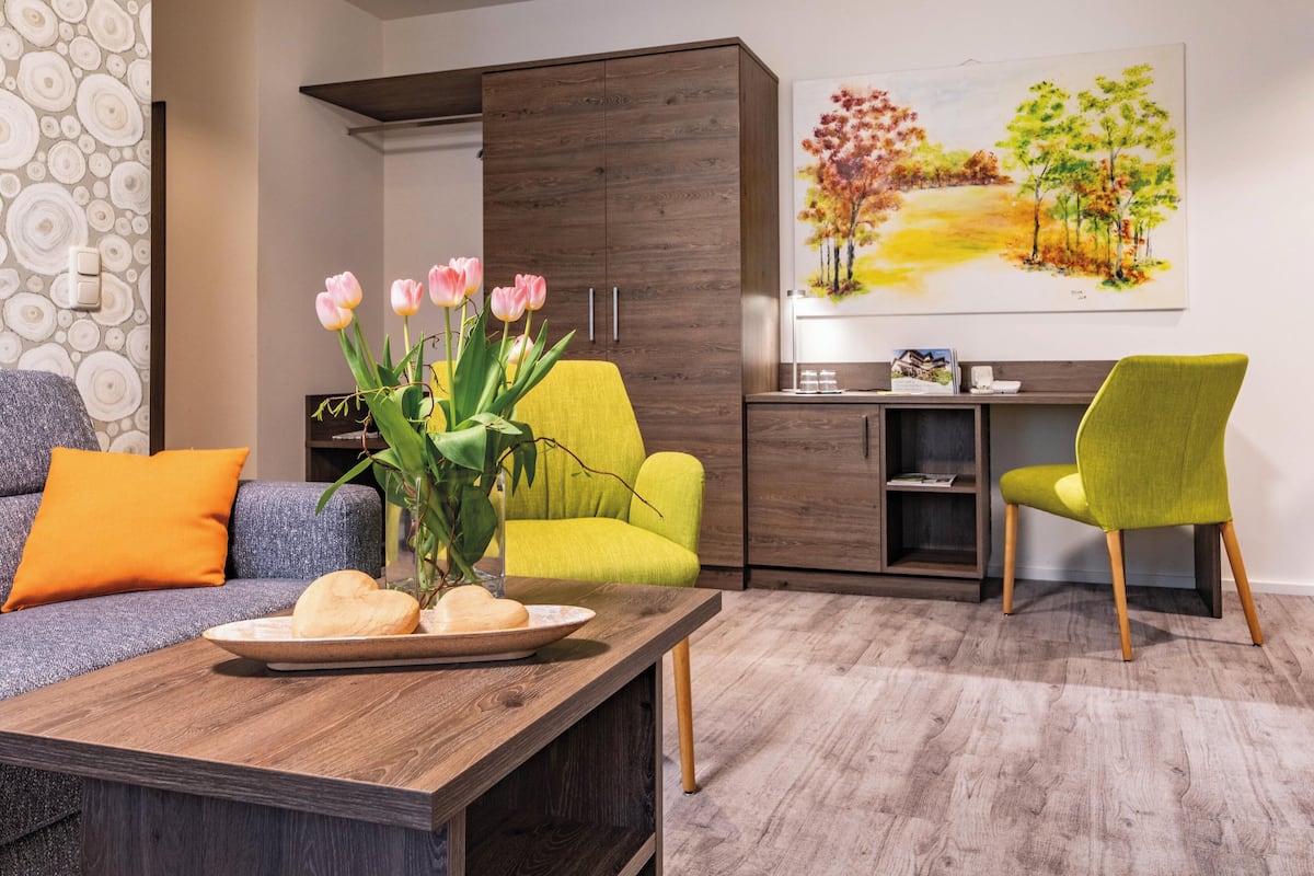 Een moderne woonkamer met een bank, een salontafel met brood, een gele fauteuil en een eethoek met een bureau en stoel.