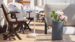 A seating area with a table and chairs, a potted plant with flowers, and a window in the background. - VitalZeit Hotel Weber (Bad Schönau)