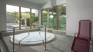 A spa room with a hot tub, large windows, and a seating area. - VitalZeit Hotel Weber (Bad Schönau)