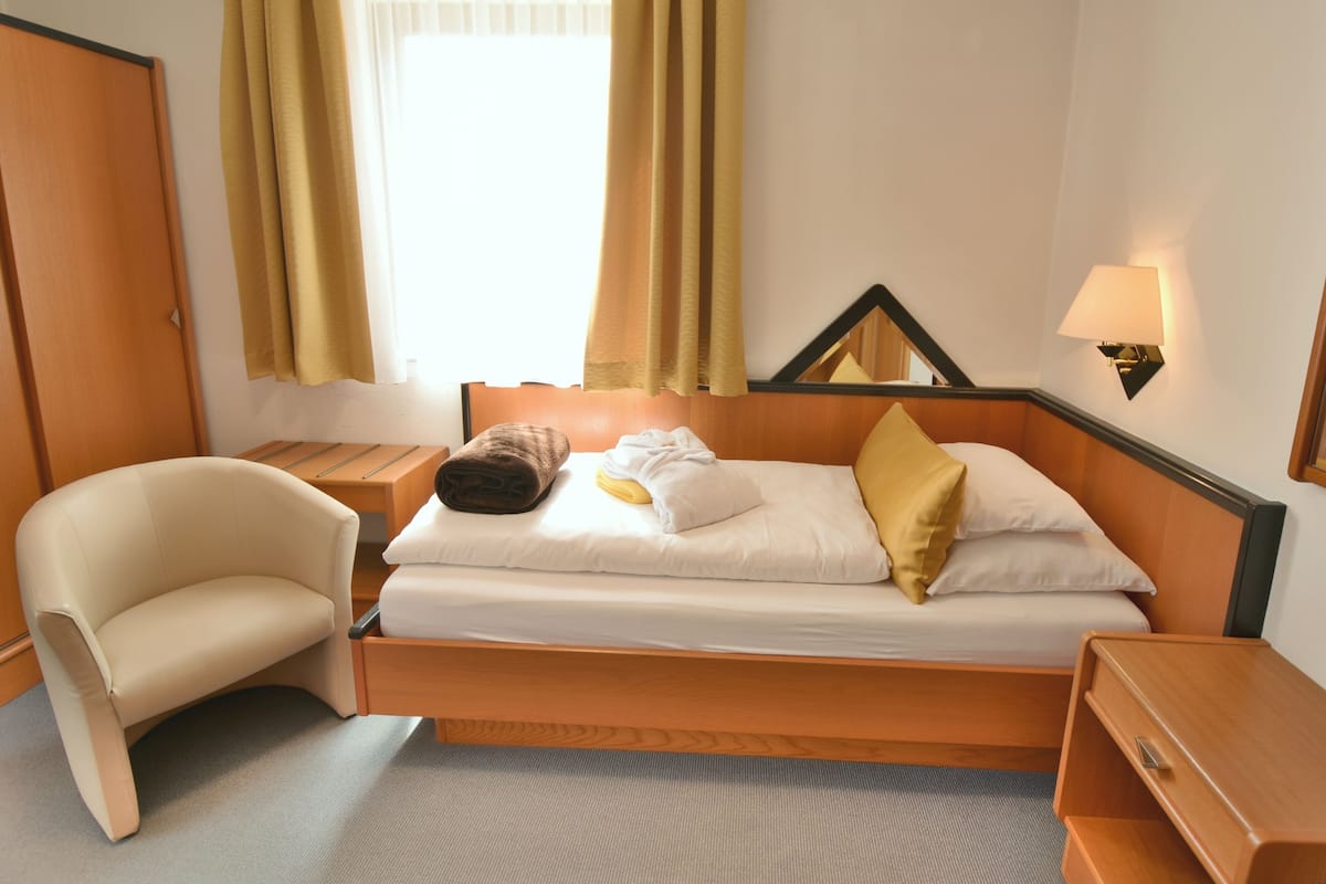 Een hotelkamer met een bed, een stoel, een nachtkastje en een lamp.