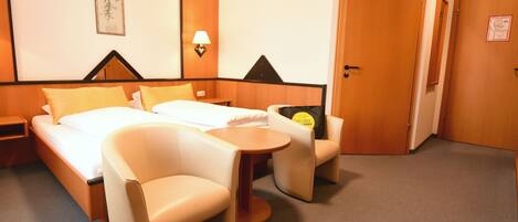 A hotel room with a bed, two chairs, a small table, a lamp, and a door.