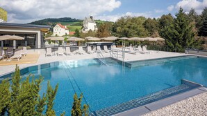 A swimming pool with lounge chairs and umbrellas, surrounded by a building and trees. - VitalZeit Hotel Weber (Bad Schönau)
