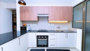 Una cocina compacta con armarios blancos, una encimera negra, una estufa, un horno y un microondas.
