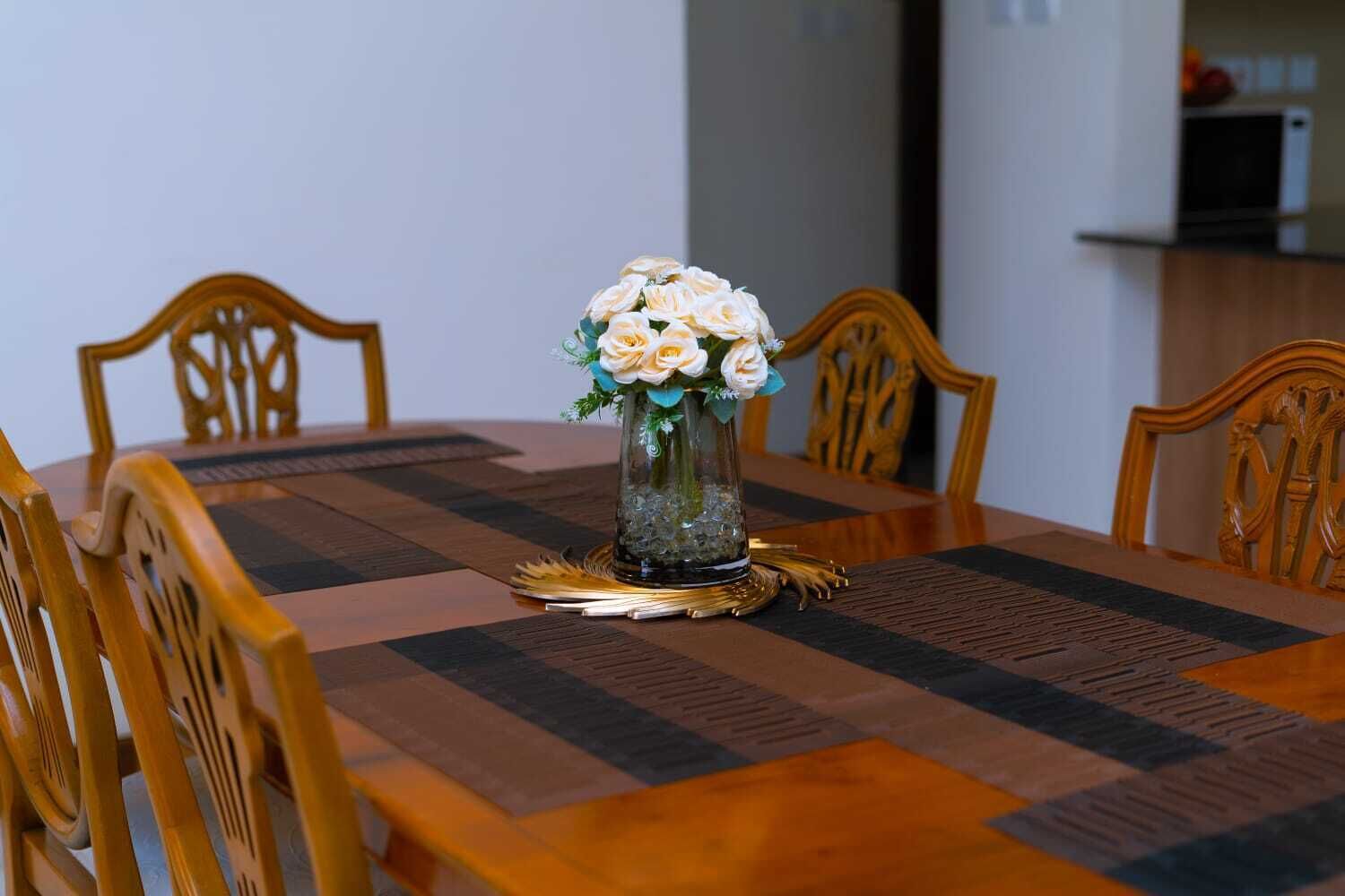 Ett matbord med en vas med blommor i mitten, omgivet av trästolar.