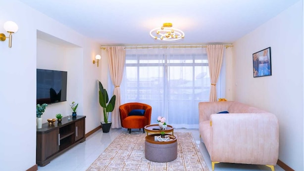 Una sala de estar con televisor, sofá, sillón, mesa de centro y un ventanal con cortinas.