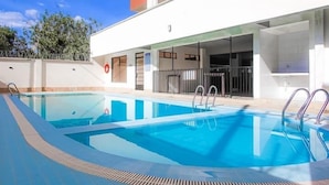 Piscina rectangular con dos juegos de escaleras metálicas en lados opuestos, rodeada por un suelo de baldosas.