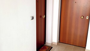 A hallway with two wooden doors, a doormat, and a light switch on the wall.