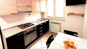 A compact kitchen with a gas stove, sink, and black cabinets. There's a window with red curtains and a flat-screen TV on the wall.