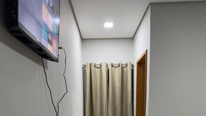 Un pasillo estrecho con una cama a la derecha, un pequeño calentador en el centro y un televisor montado en la pared.