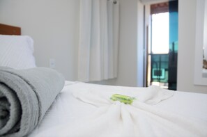 Una cama bien tendida con una toalla enrollada y una etiqueta verde sobre el sábana blanca.
