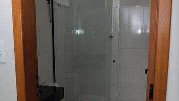 Un baño con ducha de mampara de vidrio, inodoro y lavamanos.