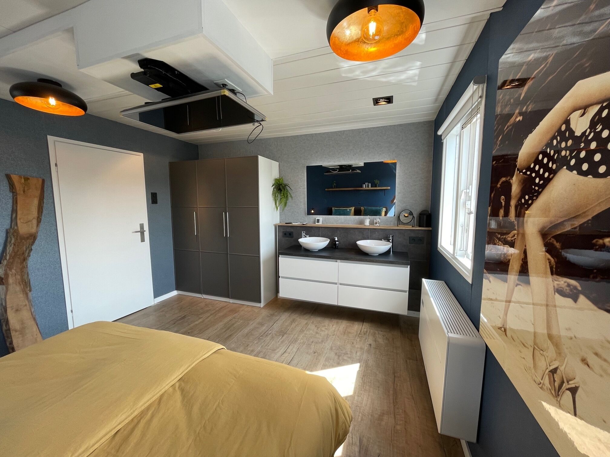 Un dormitorio moderno con cama, armario, tocador con dos lavamanos y un espejo grande.