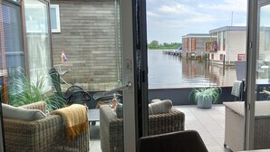 Un balcón con mobiliario de mimbre, una bandera y vistas a un canal con edificios.