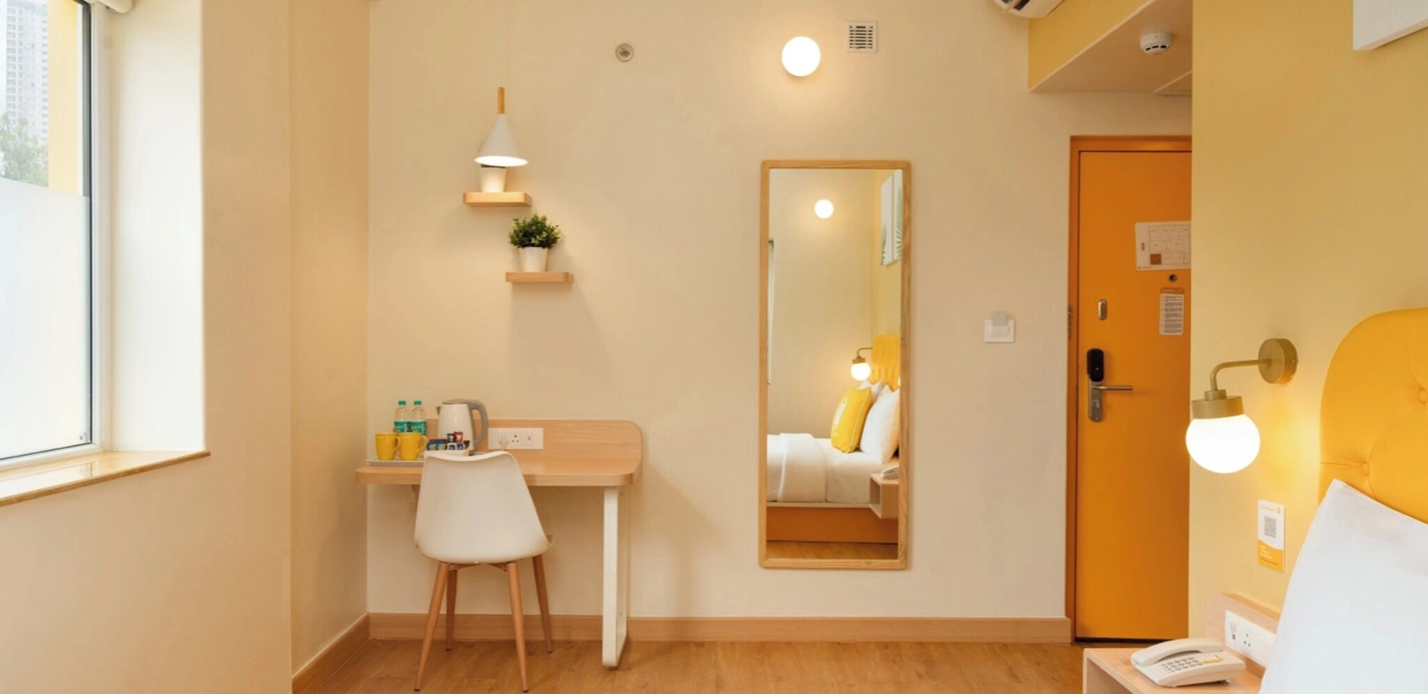 Una camera d'albergo con scrivania, sedia, comodino, lampada da comodino e specchio.