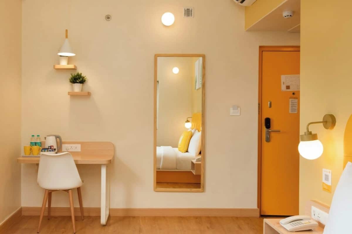 Ett hotellrum med ett skrivbord, en stol, ett nattduksbord, en sänglampa och en spegel.