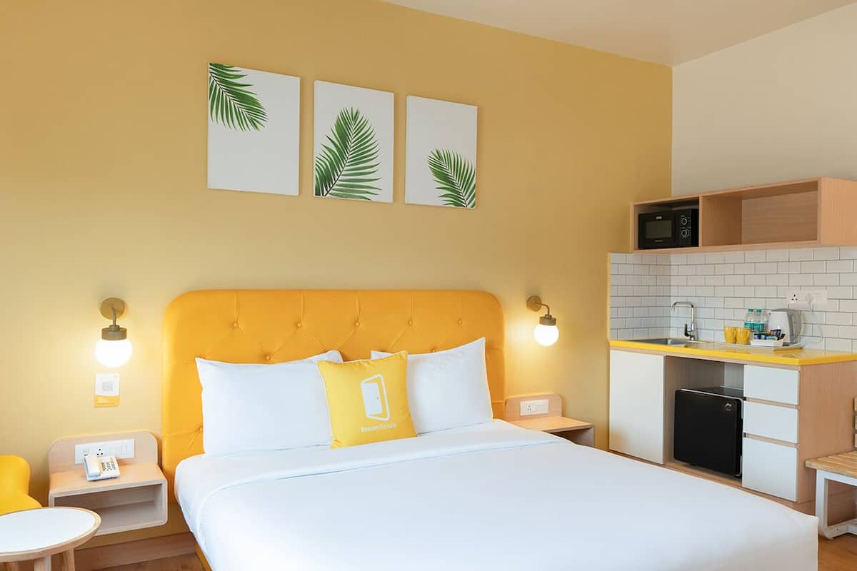 Ett hotellrum med en säng, sängbord, ett inbyggt kök och konstverk på väggen.