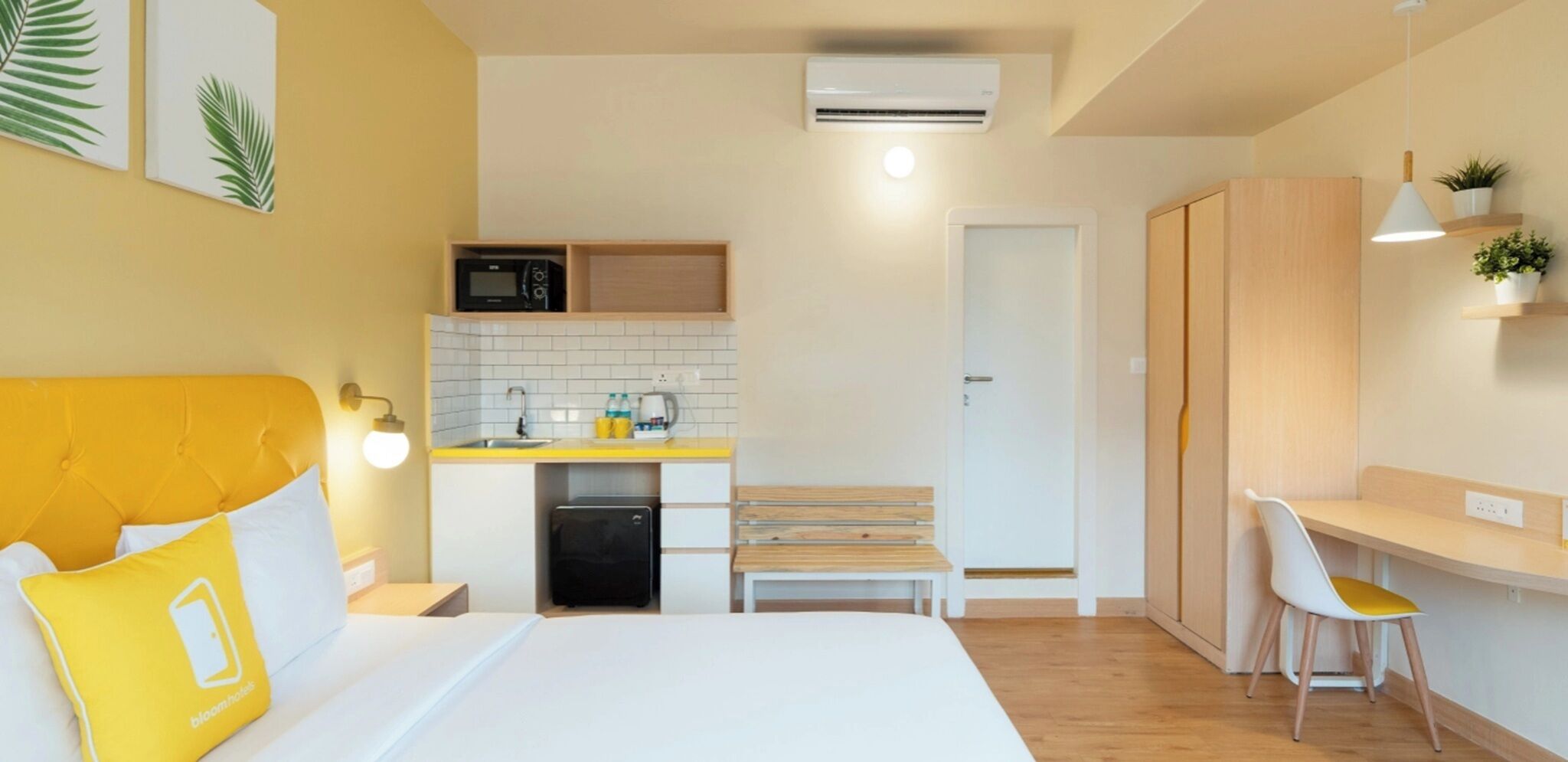 Una camera d'albergo compatta con un letto, un comodino, un angolo cottura, una scrivania con sedia e un armadio.