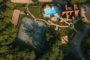Vista aérea de una propiedad con piscina, canchas de tenis y zona de estacionamiento.