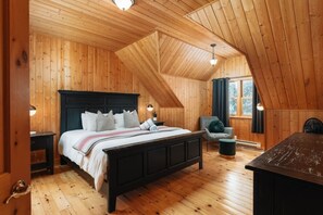 Ein Schlafzimmer in einer Holzhütte mit einem Bett, Nachttischen, einem Sessel und einem kleinen Tisch.