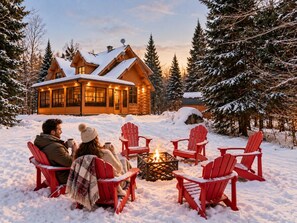 A log cabin with a fire pit and red Adirondack chairs in a snowy setting. - Serenity / SPA / Sauna / Fiddler Lake (Mille-Isles)