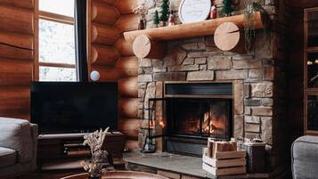 A cozy log cabin interior with a stone fireplace, a flat-screen TV, and a comfortable seating area.
