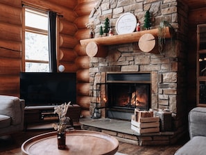 A cozy log cabin interior with a stone fireplace, a flat-screen TV, and a comfortable seating area.