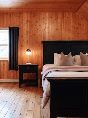 A wooden-paneled room with a bed, a nightstand, and a lamp.
