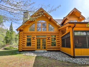 A log cabin with a symmetrical facade, large windows, and a stone chimney. - Serenity / SPA / Sauna / Fiddler Lake (Mille-Isles)