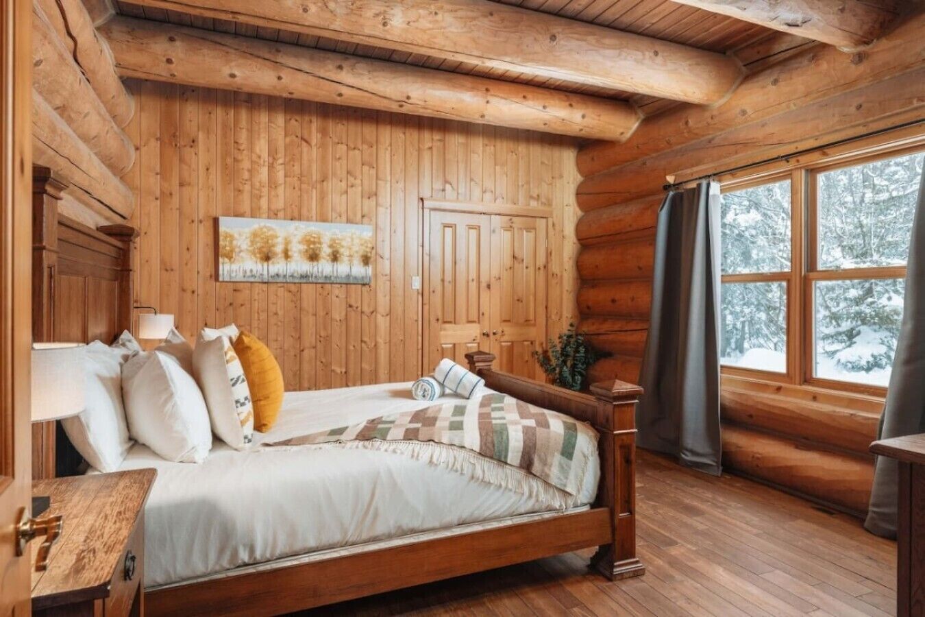 Une chambre dans une cabane en bois, avec un lit, une table de chevet et une fenêtre avec des rideaux.