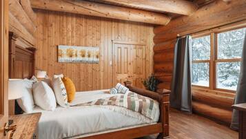 Une chambre dans une cabane en bois, avec un lit, une table de chevet et une fenêtre avec des rideaux.