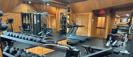 Un gimnasio con diversos equipos de ejercicio, incluyendo cintas de correr, máquinas de pesas y mancuernas.