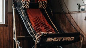 Een basketbalveld met een 'SHOT PRO' mat, een basketbalring en een houten wand.