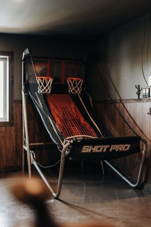 Uma quadra de basquete com um tapete da marca 'SHOT PRO', uma cesta de basquete e uma parede de madeira.