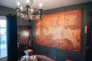 A room with a large vintage map on the wall, a chandelier, and a wooden side table.